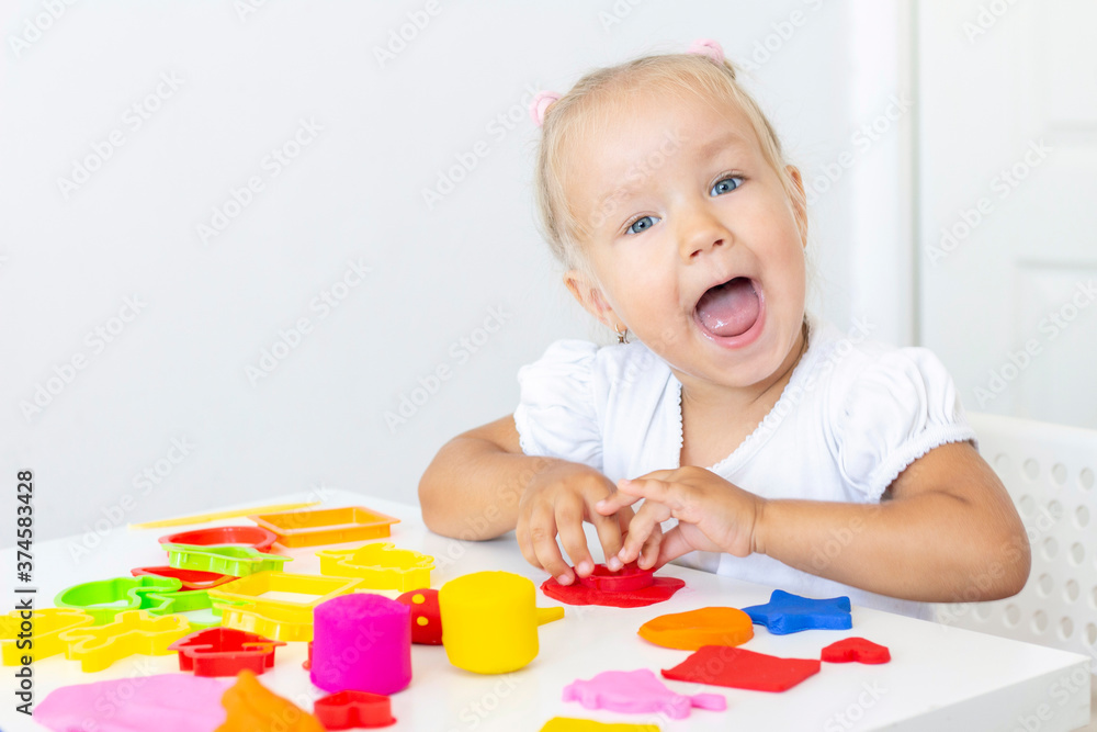 Toddler sculpts from colored plasticine on a white table. The hand of a small child squeezes pieces of colored plasticine. Childrens creativity, educational games, fine motor skills Toddler sculpts from colored plasticine on a white table. The hand of a small child squeezes pieces of colored plasticine. Childrens creativity, educational games, fine motor skills