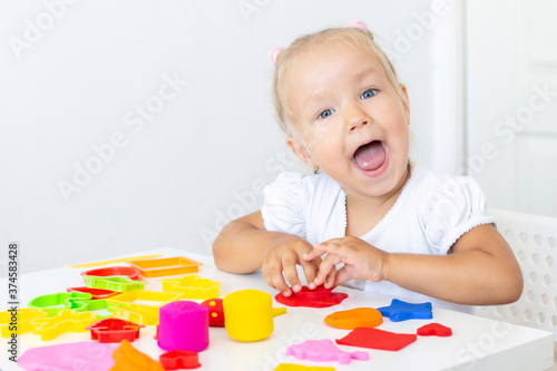 Toddler sculpts from colored plasticine on a white table. The hand of a small child squeezes pieces of colored plasticine. Childrens creativity, educational games, fine motor skills