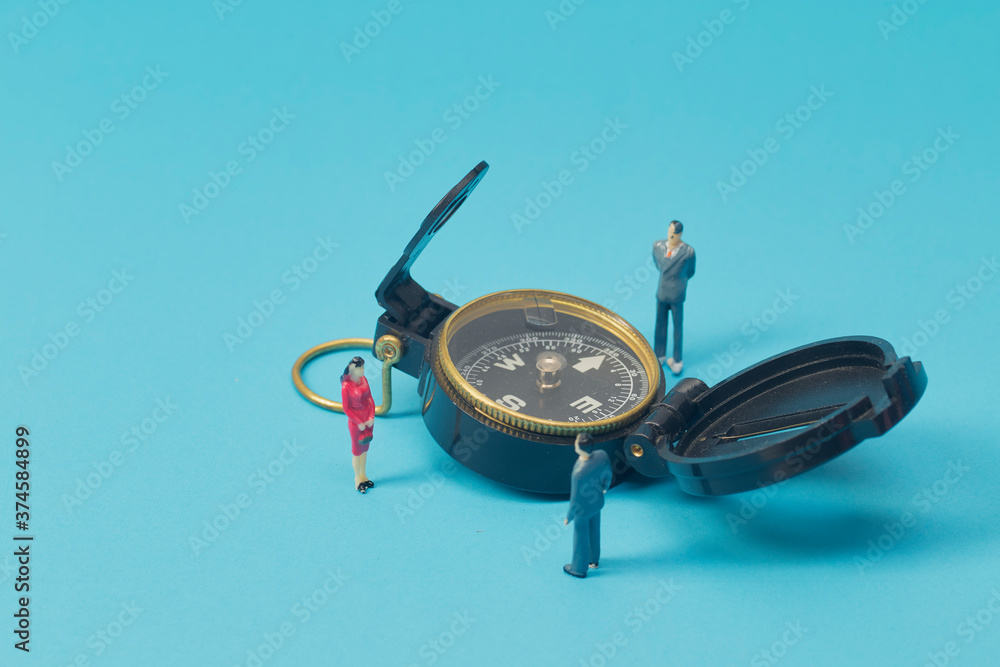 Miniature businessman and compass on blue background
