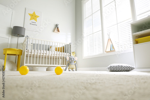 Foto Cute baby room interior with crib and big window, low angle view
