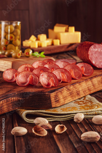 Sliced smoked salami on cutting board with cubs of cheese, olives, chestnuts and pistachios
