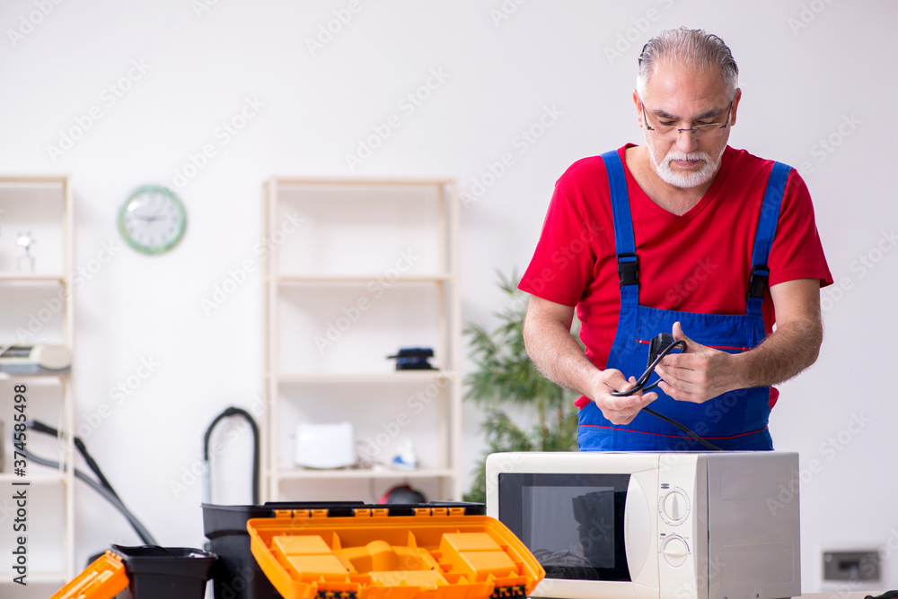 Old male contractor repairing microwave indoors Old male contractor repairing microwave indoors