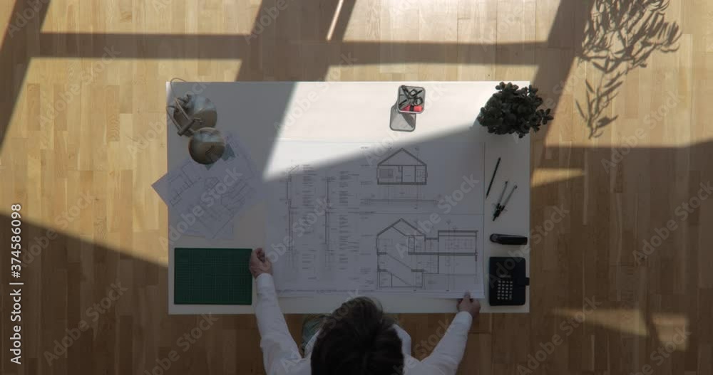 Zoom out top view shot of an architect rolling out construction plan ...