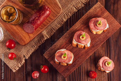 Delicious canapes with salami, cream cheese, olives and tomatos on a wooden background - Top view