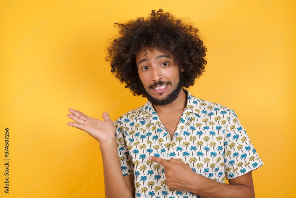 cute Young man with afro hair over wearing hawaiian shirt standing over yellow background holding hand showing advertisement cute Young man with afro hair over wearing hawaiian shirt standing over yellow background holding hand showing advertisement