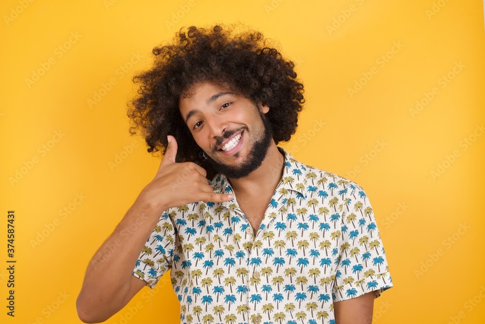 Φωτογραφία Young man with afro hair over wearing hawaiian shirt standing over yellow background smiling doing phone gesture with hand and fingers like talking on the telephone