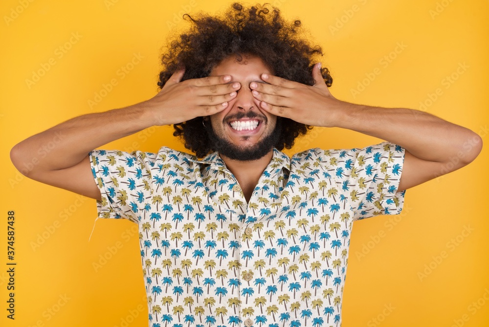 Φωτογραφία Young man with afro hair over wearing hawaiian shirt standing over yellow background covering eyes with hands smiling cheerful and funny