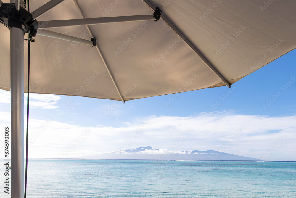 An umbrella provides shade on a tropical island beach with turquoise water