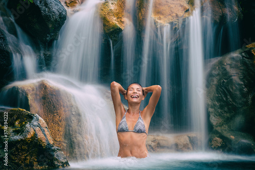 Waterfall woman in bikini smiling happy in natural pool on travel. Sexy beautiful girl in pristine nature enjoying summer travel vacation.