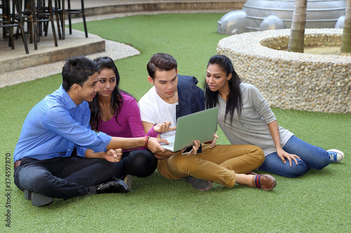 group of Asian young man woman friend student colleagues sting on green grass talk mingle discuss study computer laptop