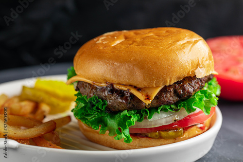 Delicious juicy and spicy burger with slice of tomato, onion, and cheese. Served with fries and pickles.