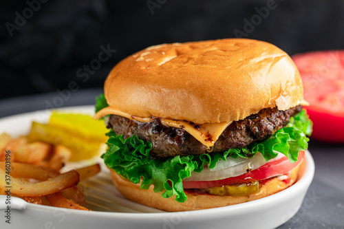 Delicious juicy and spicy burger with slice of tomato, onion, and cheese. Served with fries and pickles.
