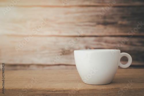 A white hot coffee cup with the light shines from the top down the cup is placed on a wooden plate and on a wooden background.