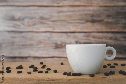 A white hot coffee cup with coffee beans are placed on a wooden plate and on a wooden background.