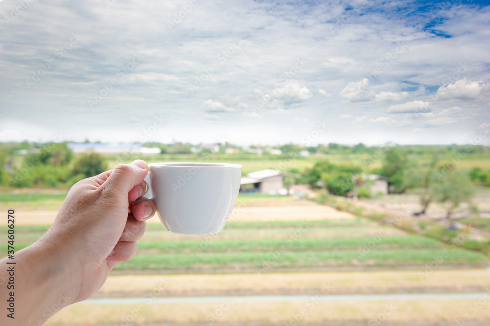 A white man's hand holding a hot coffee cup on the landscape field nature background.