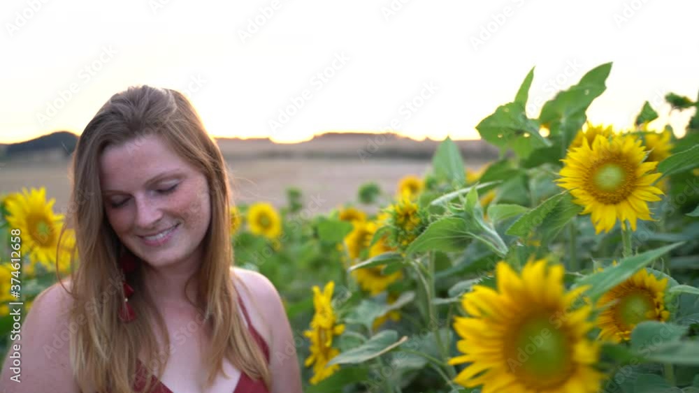 Smiling Caucasian woman with blond hair smelling sunflower in farm on sunny day Smiling Caucasian woman with blond hair smelling sunflower in farm on sunny day