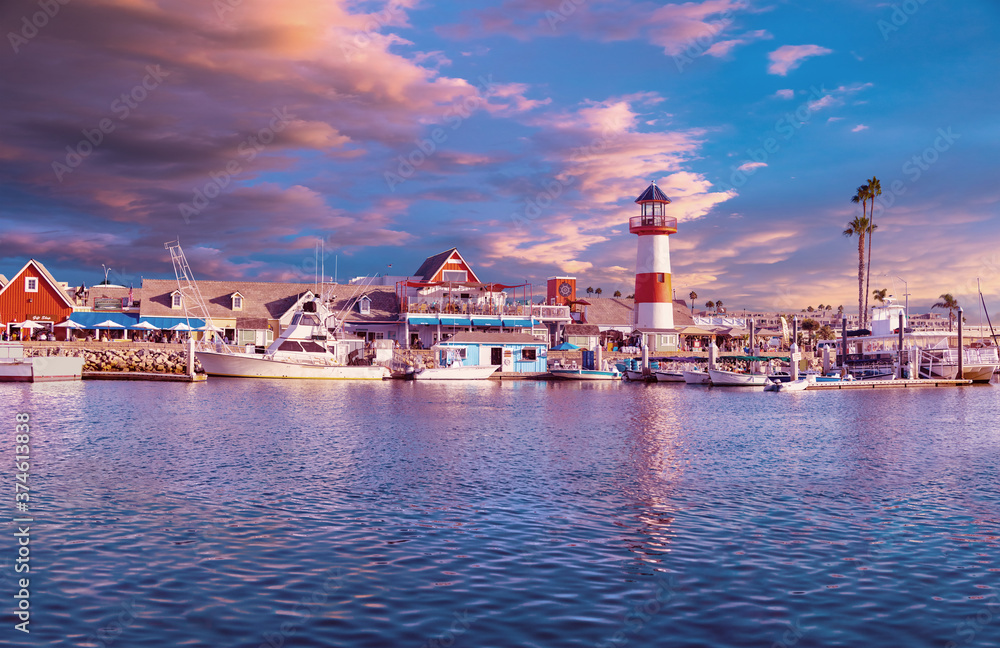 Colorful panorama of Oceanside Harbor at sunset with sky, waterfront and lighthouse reflected in the harbor.