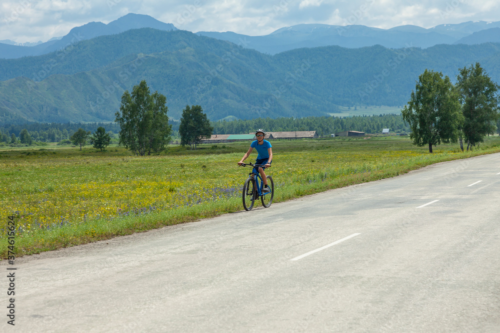 A young cyclist rides a mountain bike along a mountain road past against the backdrop of picturesque blue mountains. A young cyclist rides a mountain bike along a mountain road past against the backdrop of picturesque blue mountains.