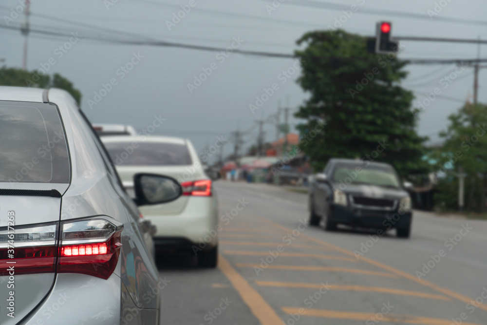 Fototapeta premium Close up on rear of silver car stopped on an asphalt road at an intersection. With yellow line in center of the road. And the blur of the car across the road.