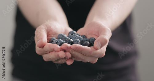 man hands show wet washed ripe blueberries on neutral background