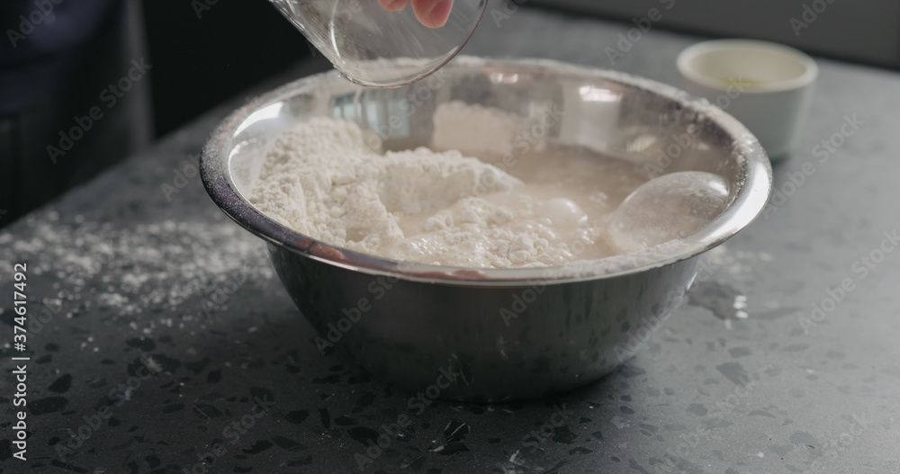 wet ingredients into flour in steel bowl on concrete countertop