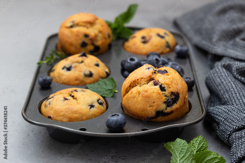 Freshly baked blueberry muffins with thyme and mint in a muffin tin. Grey background. Freshly baked blueberry muffins with thyme and mint in a muffin tin. Grey background.