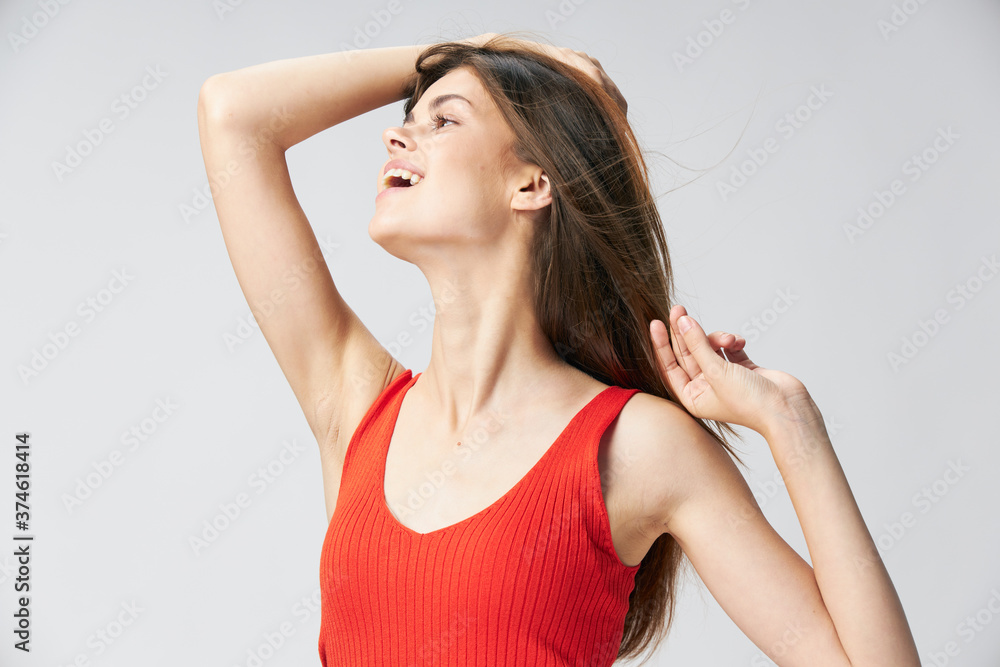 Happy woman in a red T-shirt touches the hair on her head with her hand and looks to the side 