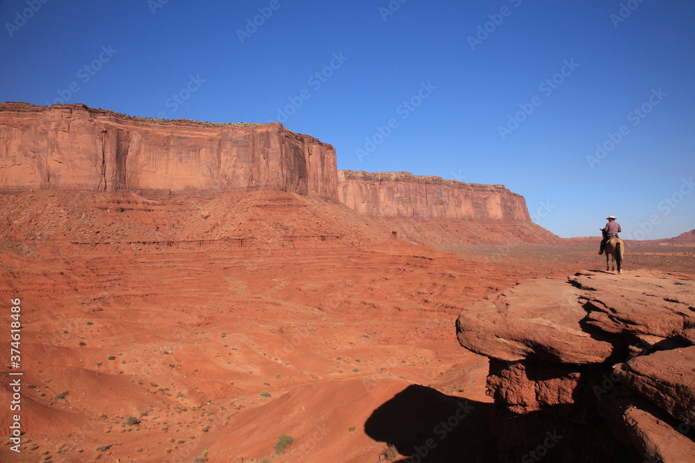 Western Cowboy riding on Horse from John Ford's Point overlook in Monument Valley Tribal Park with the mittens and Merrick Butte in Arizona, USA Western Cowboy riding on Horse from John Ford's Point overlook in Monument Valley Tribal Park with the mittens and Merrick Butte in Arizona, USA