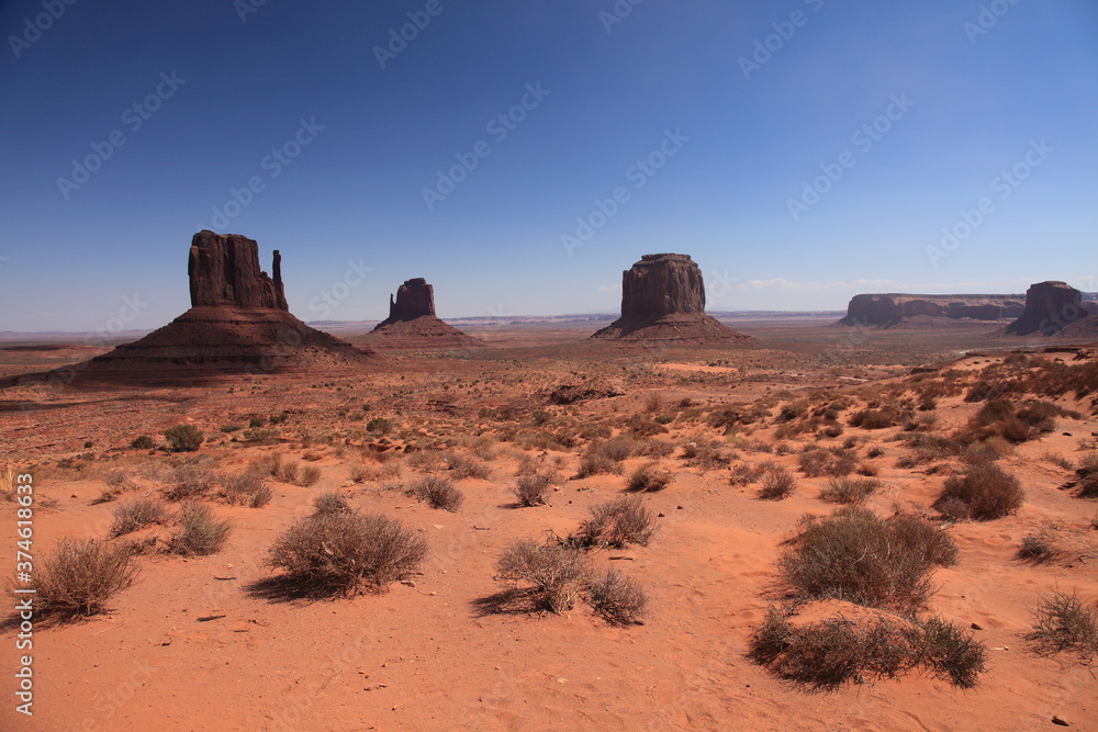 View of The mittens and Merrick Butte in Monument Valley tribal park under blue sky in Arizona, USA