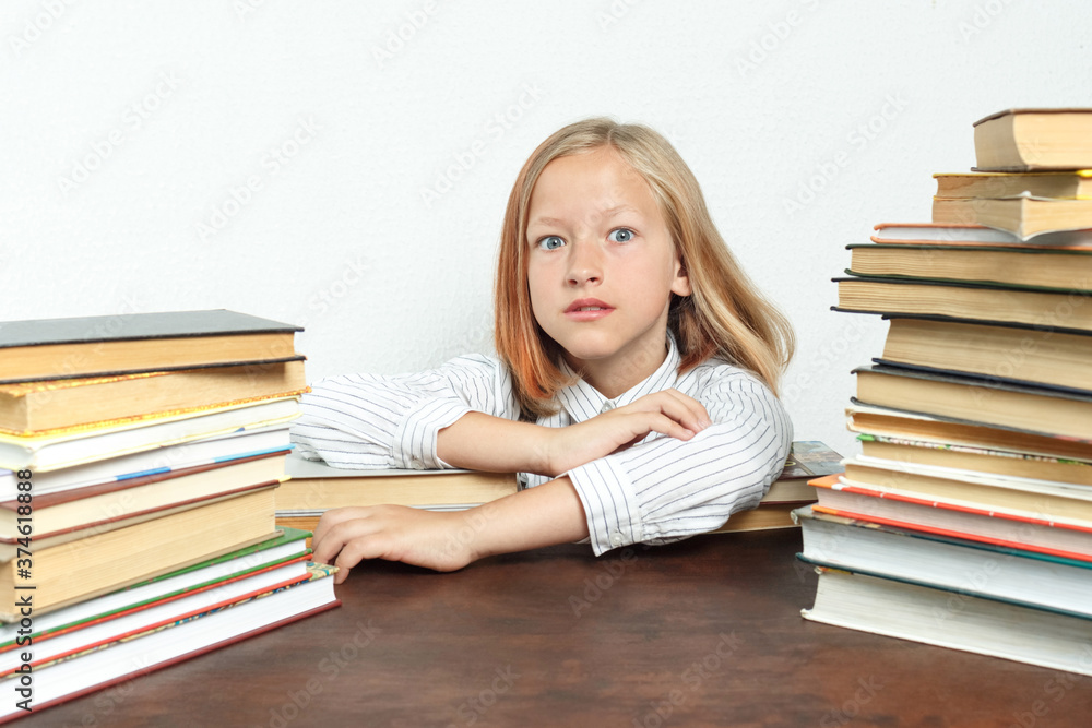 Portrait of a teenage girl who sits at a table among the books. Looks into the camera. Isolated background. Portrait of a teenage girl who sits at a table among the books. Looks into the camera. Isolated background.