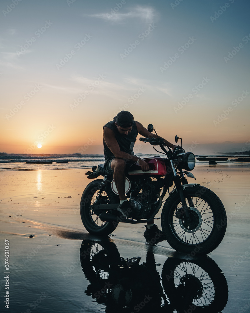 Fototapeta premium Male model on a custom bike during sunset in the beach