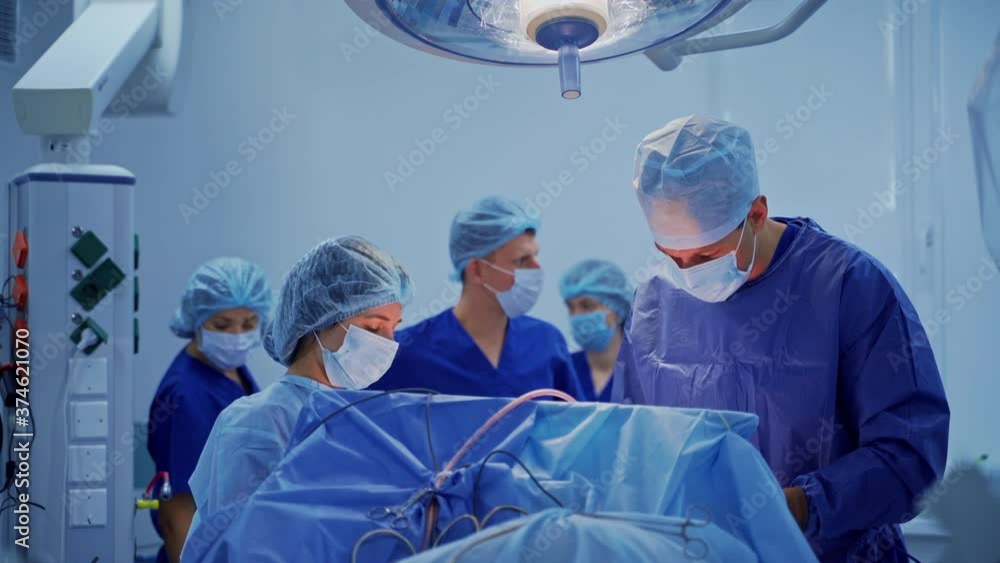 Group of medical specialists in surgical room. Doctors in blue uniform conduct a surgery under the medical lamp. Health care concept. Group of medical specialists in surgical room. Doctors in blue uniform conduct a surgery under the medical lamp. Health care concept.