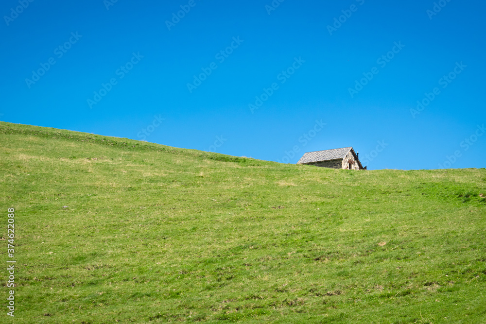 Glimpse of an old hut beyond a grassy hill, clear blue sky. Sunny day on the Piani dell'Avaro, Val Brembana, Bergamo, Italy. Typical mountain landscape on a summer day. Minimal composition Glimpse of an old hut beyond a grassy hill, clear blue sky. Sunny day on the Piani dell'Avaro, Val Brembana, Bergamo, Italy. Typical mountain landscape on a summer day. Minimal composition