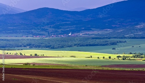 Top view on Stara Planina: Carpathian mountains and a small village in the background, green meadow in summer against cloudy sky in Bulgaria.