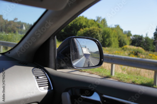 Indoor to outdoor from car view in front side window to back view mirror with boat on trailer and natural landscape reflection, car trip active vacation in Russia on Sunny summer day © Ilya