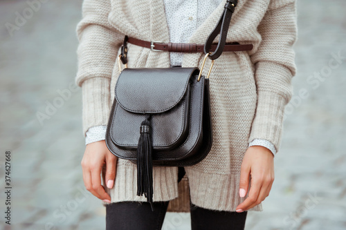 Fashionable young woman in black jeans, beige cardigan and black handbag . Street style