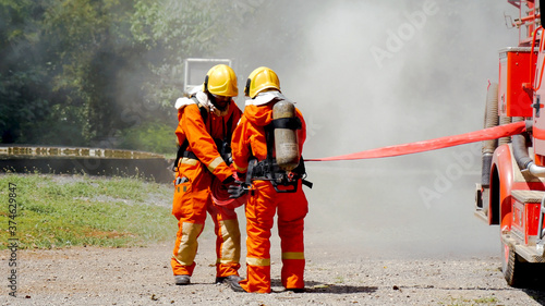 Firefighter fighting with flame using fire hose chemical water foam spray engine. Fireman wear hard hat, body safe suit uniform for protection. Rescue training in fire fighting extinguisher