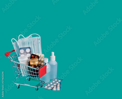 Medicine bottles with pills and medical masks in a shopping cart on a green background. Copy space.