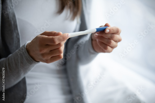 Close up cropped image woman holding plastic pregnancy test kit in hands  sitting on bed at home  young female checking results  fertility maternity concept  gynecological healthcare