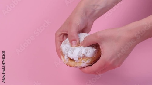 Break a round donut with a filling with your hands. Condensed milk inside. Lots of powdered sugar. Pink background. Delicious food.