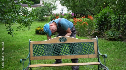 Gardener man disassemble retro bench in garden yard. Outdoor furniture renew