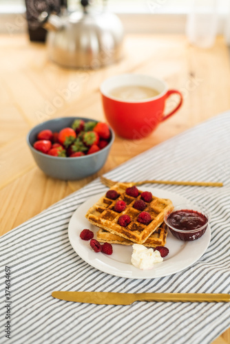 Belgian waffles for breakfast. Waffles with fresh berries and berry jam. Cup of coffee and teapot on the table. Breakfast in the trailer