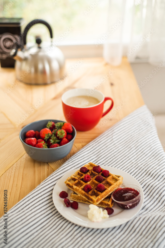 Belgian waffles for breakfast. Waffles with fresh berries and berry jam. Cup of coffee and teapot on the table. Breakfast in the trailer Belgian waffles for breakfast. Waffles with fresh berries and berry jam. Cup of coffee and teapot on the table. Breakfast in the trailer