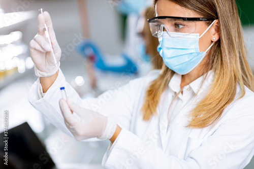 Woman doctor wearing protective face mask in lab hold needle syringe and medicine vial vaccine bottle