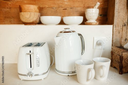 White toaster, kettle and two cups on the kitchen table. Light and modern kitchen details