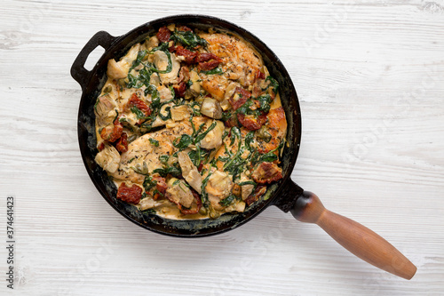 Homemade Creamy Tuscan Chicken in a cast iron pan on a white wooden background, top view. Flat lay, overhead, from above.