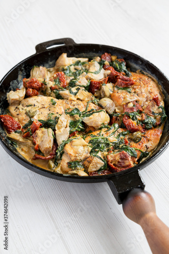 Homemade Creamy Tuscan Chicken in a cast-iron pan on a white wooden surface, low angle view.
