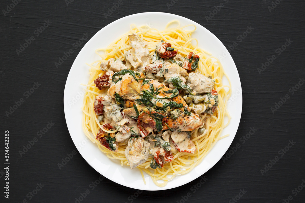 Homemade Creamy Tuscan Chicken with Pasta on a white plate on a black background, side view. Close-up.