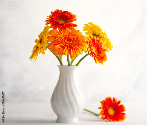 Beautiful bouquet of red and yellow flowers in white vase on wooden table, front view. Autumn still life with flowers.