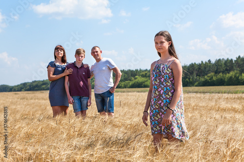 Fototapeta Concept of adopted kid, pretty girl standing on foreground with adoptive family